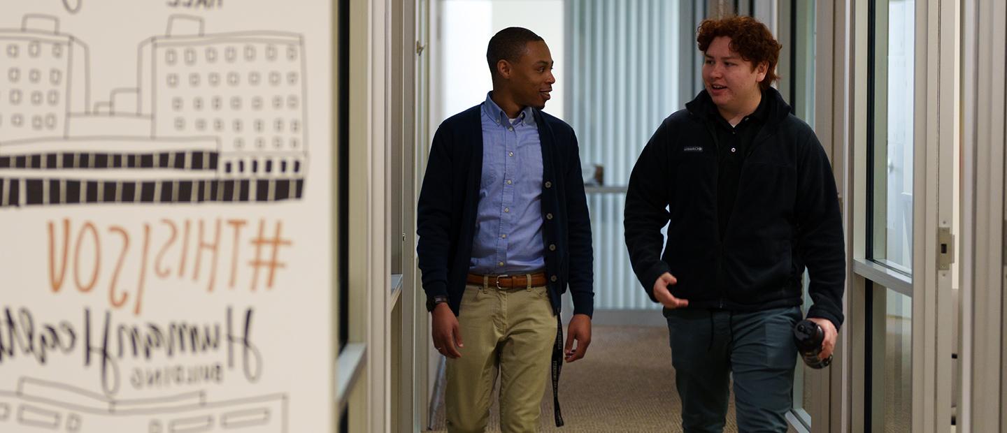 两个年轻人一起走在北大校园一栋大楼的走廊上.